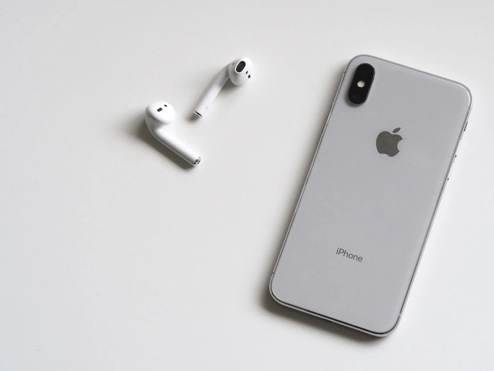 iPhone X argenté avec AirPods illustrant le fonctionnement Bluetooth entre smartphone et écouteurs sans fil
